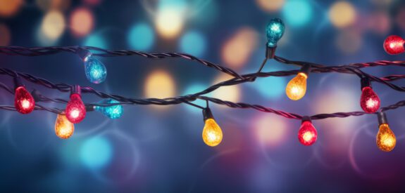 Close-up of colorful string lights with red, blue, yellow, and green bulbs, glowing against a blurred background of multicolored lights, creating a festive and cheerful atmosphere.