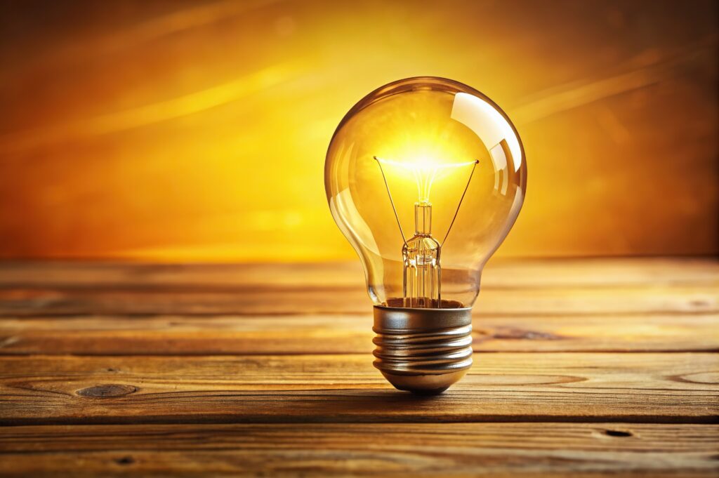 Lightbulb on a wooden surface with a glowing, yellow background.